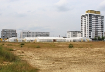 Die Gebäude und ihr noch unbebautes Umfeld, vorn eine Flüchtlingsnotunterkunft
